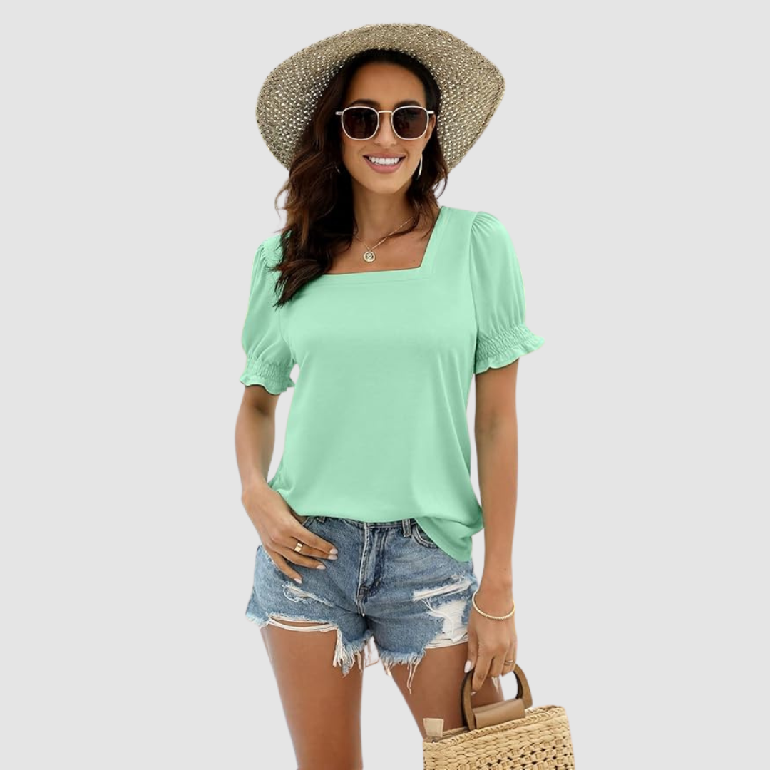 Woman wearing mint green square neck top with puffed sleeves, denim shorts, straw hat, and woven handbag on studio background.