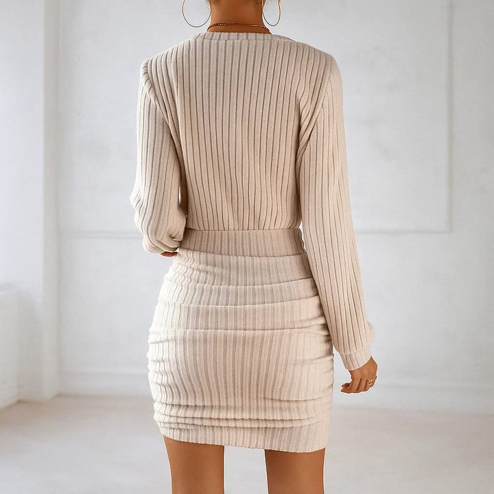 Back view of beige knit dress with ribbed texture, showing fitted silhouette, worn indoors in bright room.