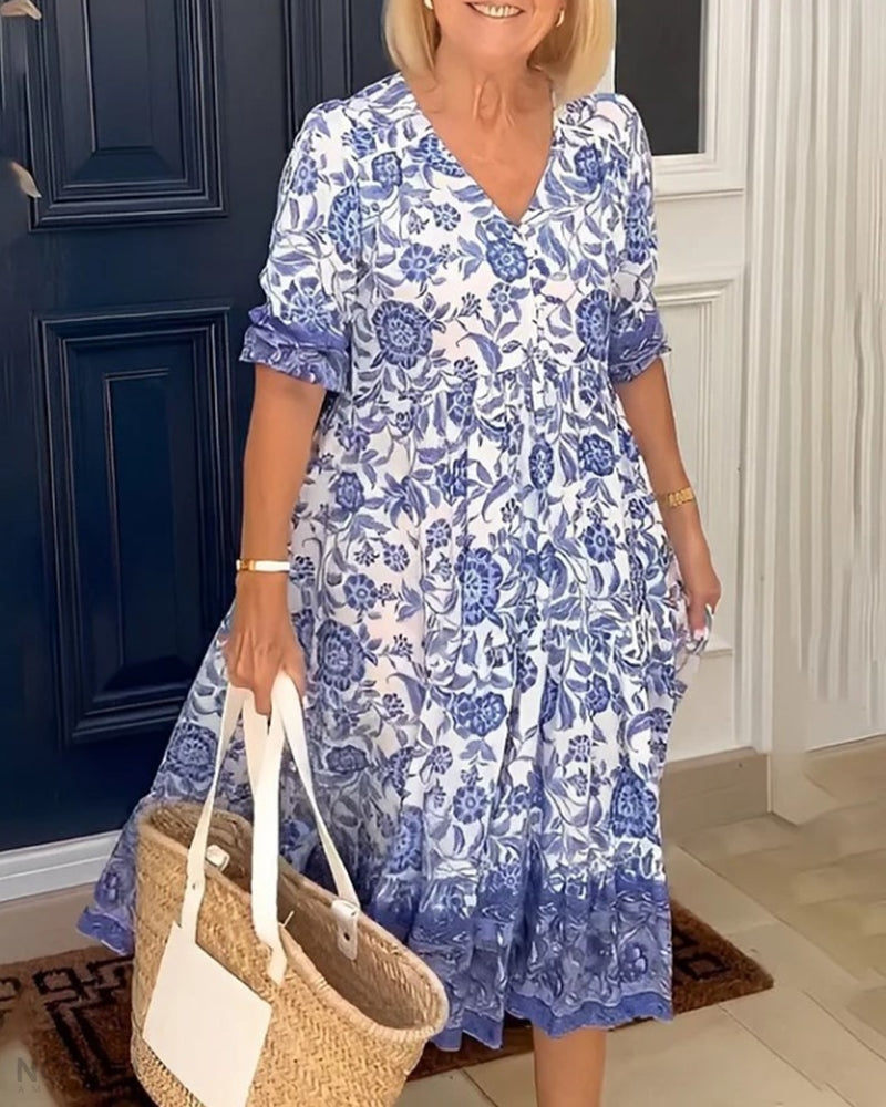 Woman wearing a blue floral V-neck dress with a straw bag, in front of a blue door.