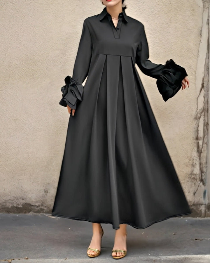 Elegant black maxi dress with long sleeves and flared design against a textured neutral wall.