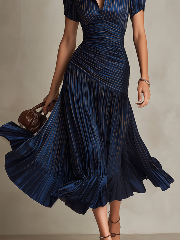 Close-up of model in navy midi dress with pleated skirt and ruched waist, holding a purse in a studio.