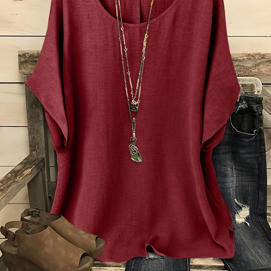 Burgundy loose summer top on hanger with necklace, sandals, and jeans on rustic bench.