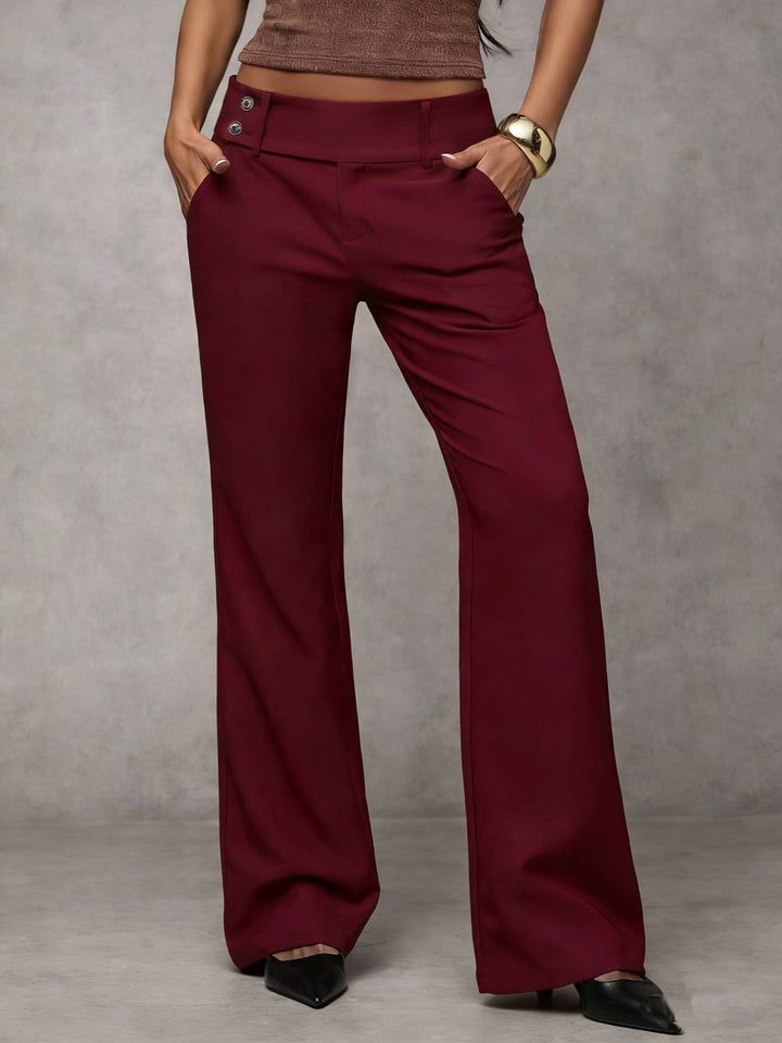 Burgundy modern pants with button detail, modeled with hands in pockets. Indoor gray background.