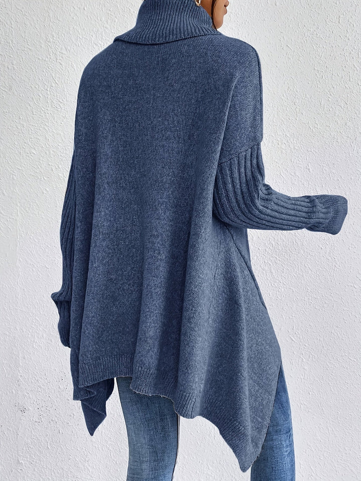 Back view of blue turtleneck sweater with long ribbed sleeves, styled with jeans, in front of a white wall.