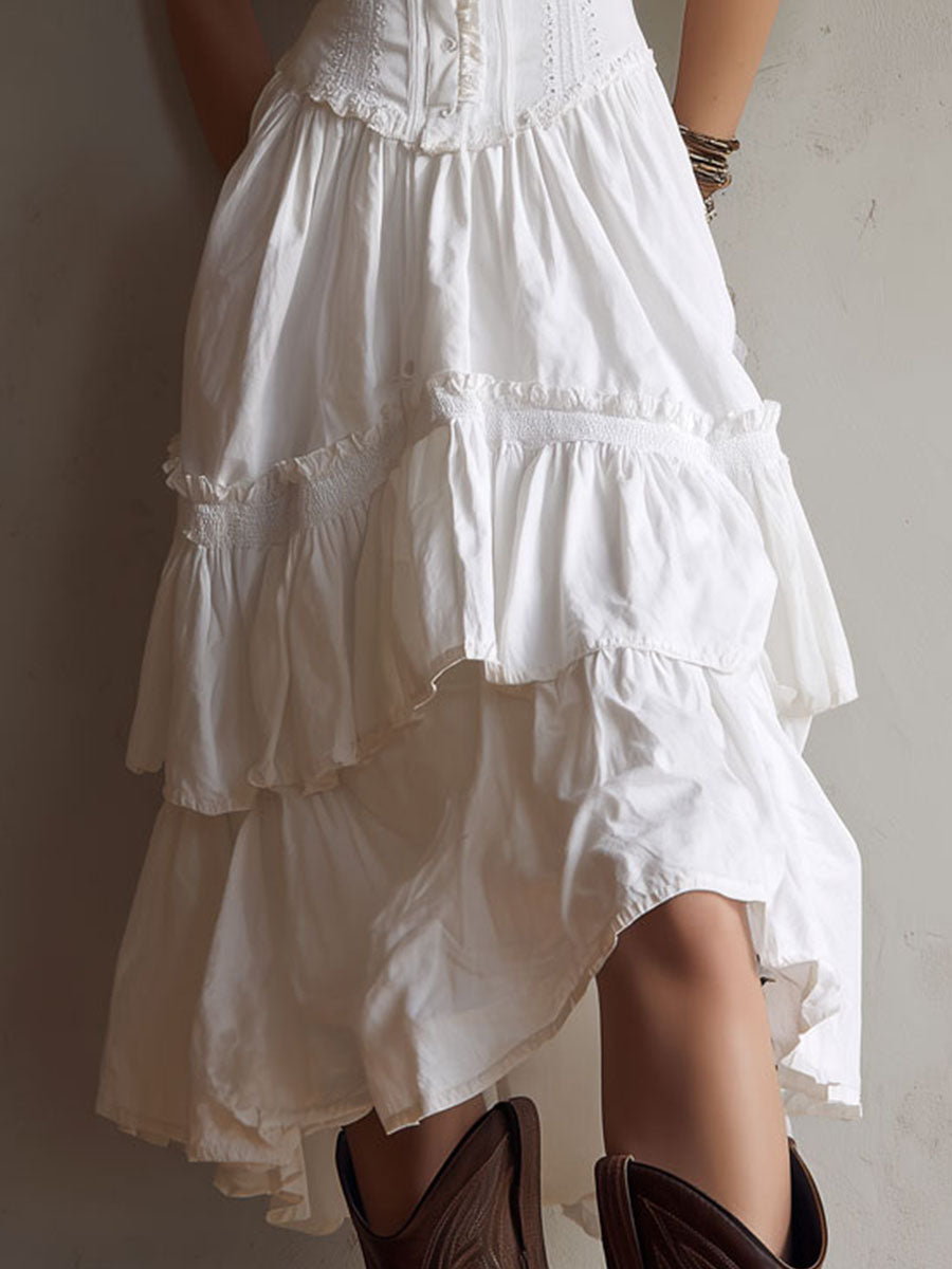 Close-up of white midi dress skirt with tiered ruffles. Brown boots, neutral background.