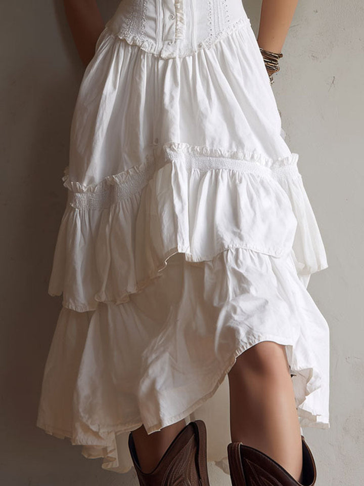 Close-up of white midi dress skirt with tiered ruffles. Brown boots, neutral background.
