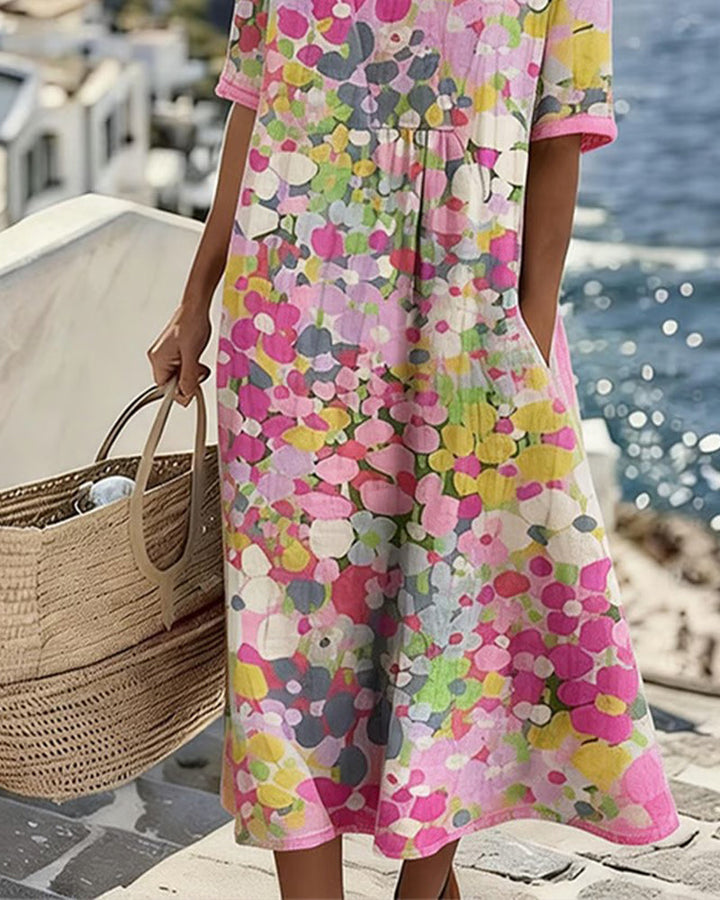 Focus on floral printed midi dress, model holding wicker bag on seaside terrace with ocean backdrop.