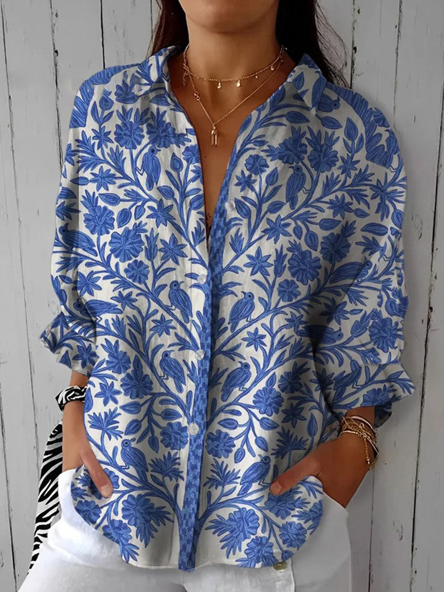 Woman wearing a blue floral patterned blouse with a relaxed fit, standing against a rustic wooden backdrop.