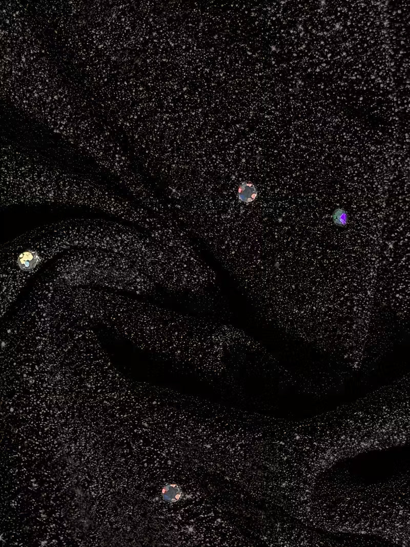 Detailed view of black dress fabric featuring sparkling dots and folds, showcasing texture and shine.
