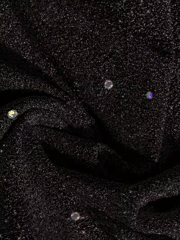 Detailed view of black dress fabric featuring sparkling dots and folds, showcasing texture and shine.