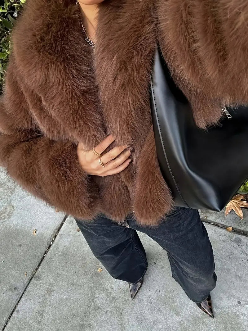 Close-up of a plush brown fur jacket paired with dark pants and a black bag, worn by a person standing on a sidewalk.