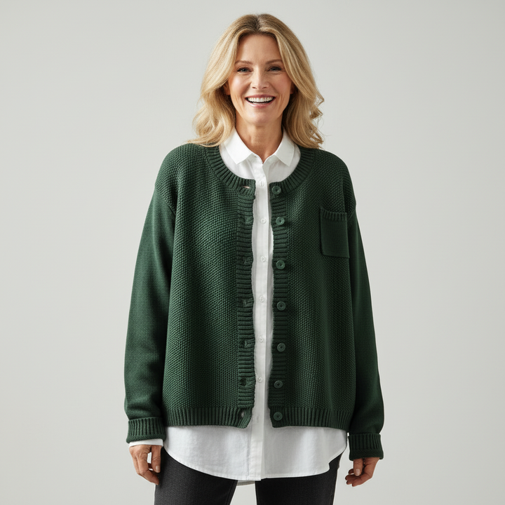 Woman in studio wearing dark green knit cardigan over white shirt, smiling.