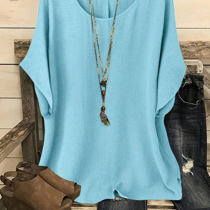 Turquoise loose summer top on hanger with necklace, sandals, and jeans on rustic bench.