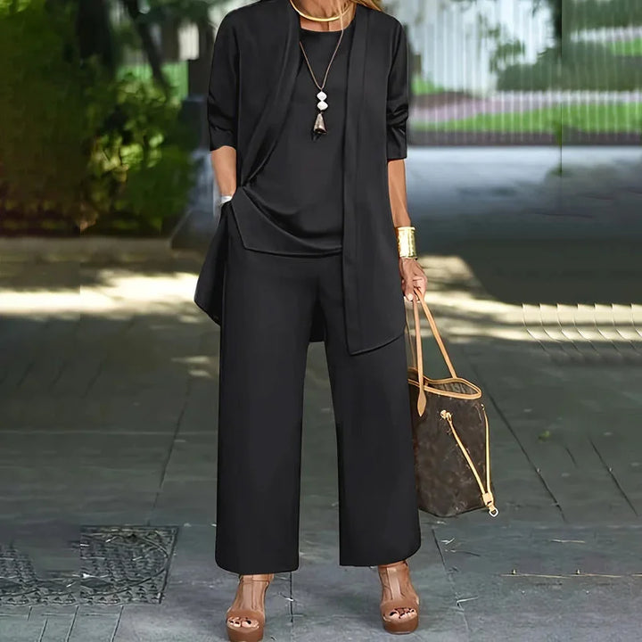 Black three-piece set with flowing top, open-front jacket, and wide-leg pants. Outdoors, woman holding a handbag.