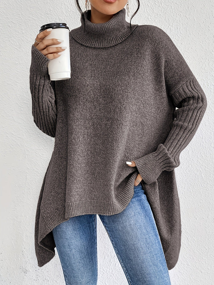 Brown turtleneck sweater with ribbed sleeves, holding a coffee cup, paired with jeans against a white background.