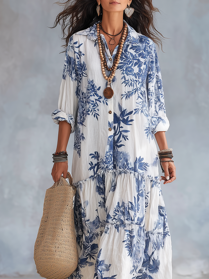 White dress with blue floral pattern, featuring layered accessories and a woven bag. Soft, artistic studio backdrop.