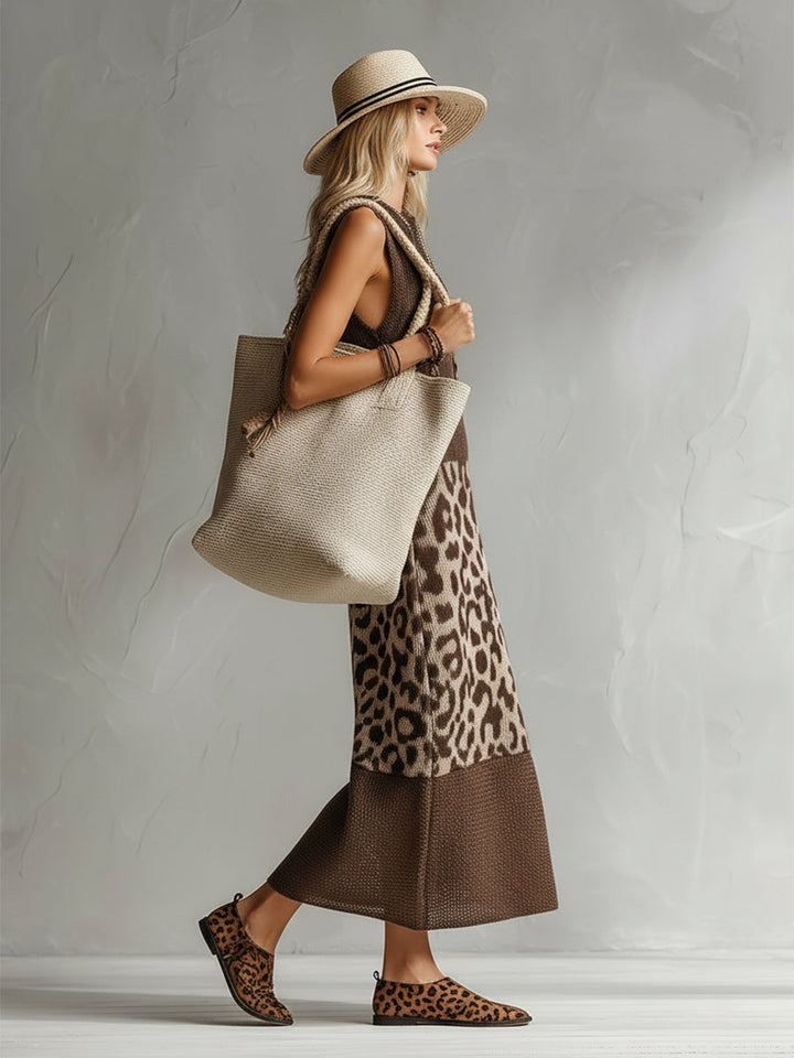 Side view of a woman wearing a sleeveless knitted leopard print dress and hat, carrying a textured tote bag, in a studio setting.