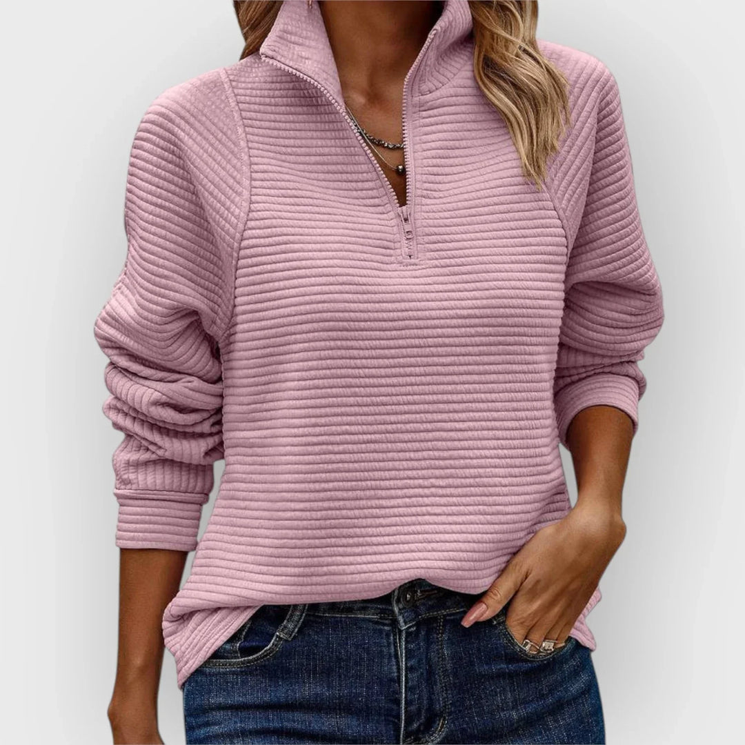 Woman wearing a light pink half-zip pullover with ribbed texture, paired with jeans, against a plain background.