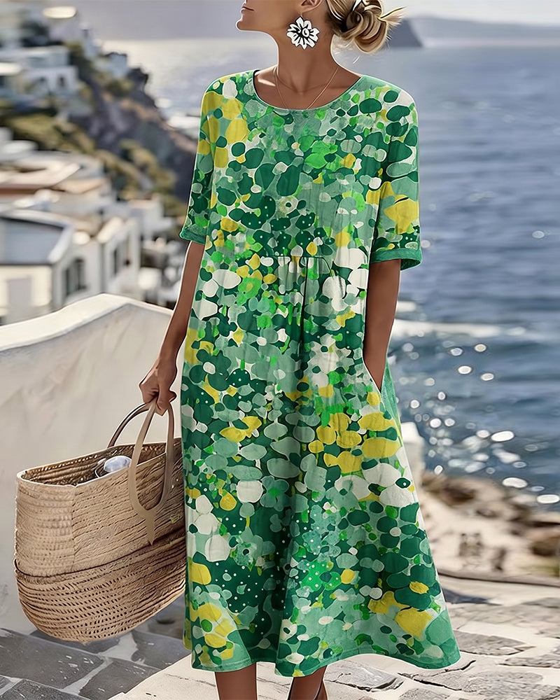 Model in green and yellow floral midi dress, holding bag on terrace with ocean view.