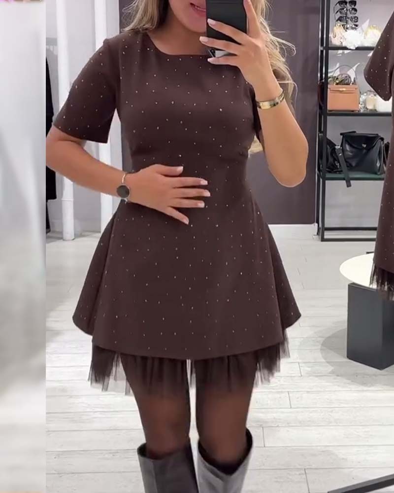Woman in brown dress with stud embellishments and tulle hem, hand on waist. Studio setting with light floors.