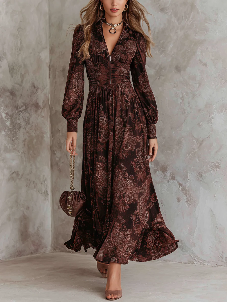Woman wearing a paisley-patterned, dark-colored maxi dress with a zip front, long sleeves, and a flowy hem. Styled in an indoor setting with a textured wall backdrop.