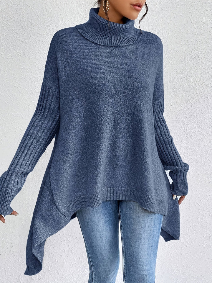 Blue turtleneck sweater with long sleeves and subtle knit pattern, paired with jeans, set against a plain white wall.