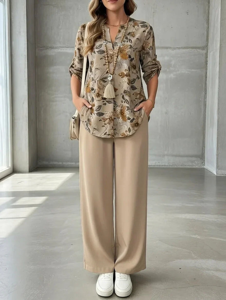 Floral top with rolled sleeves and beige pants, worn by a person in a well-lit room with a concrete wall.