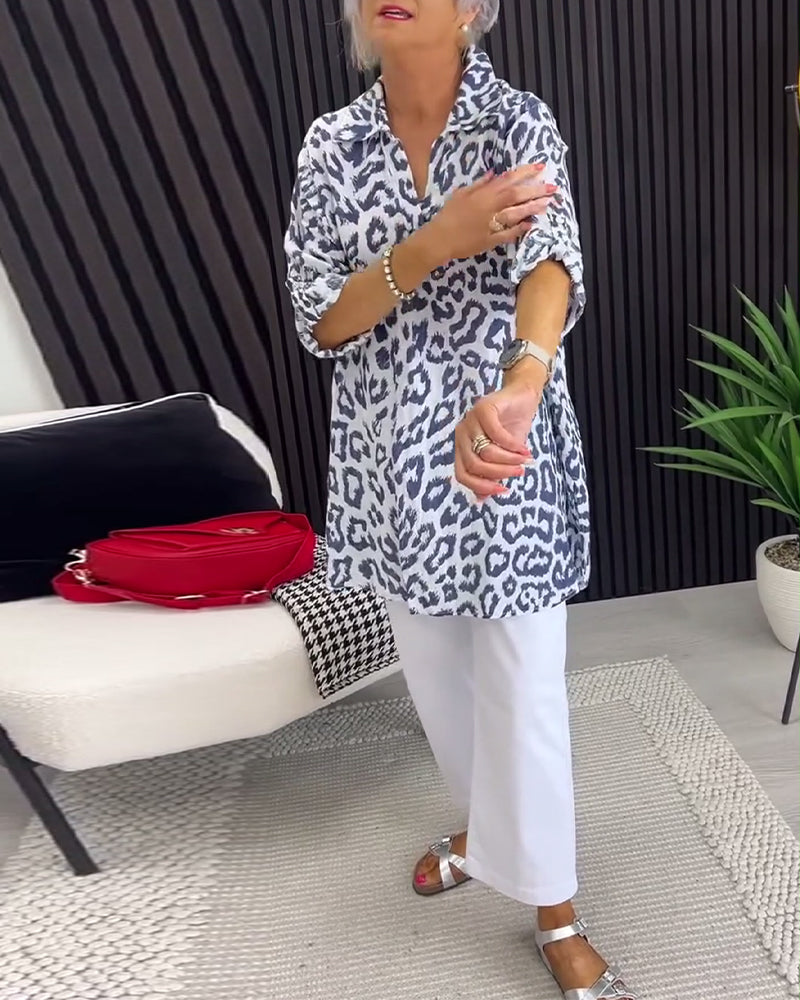 Black leopard print blouse with collar, worn with white pants, in a modern indoor setting featuring a plant and decor.