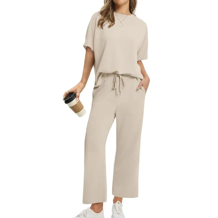 Woman wearing an elegant beige set with loose top and drawstring pants, holding a coffee, in a studio setting.