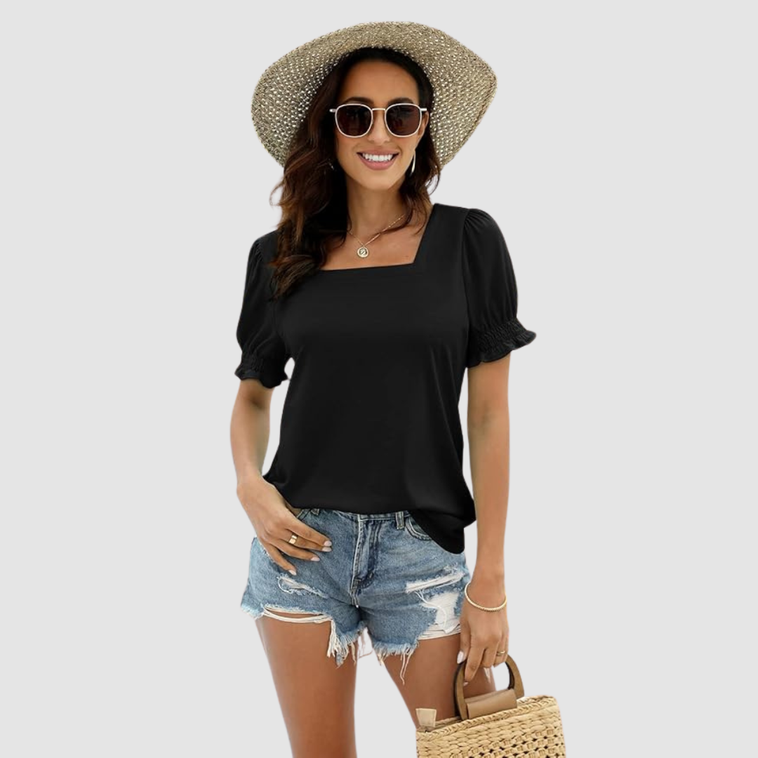 Model in black square neck top, denim shorts, sunglasses, straw hat, and wicker bag against plain studio backdrop.