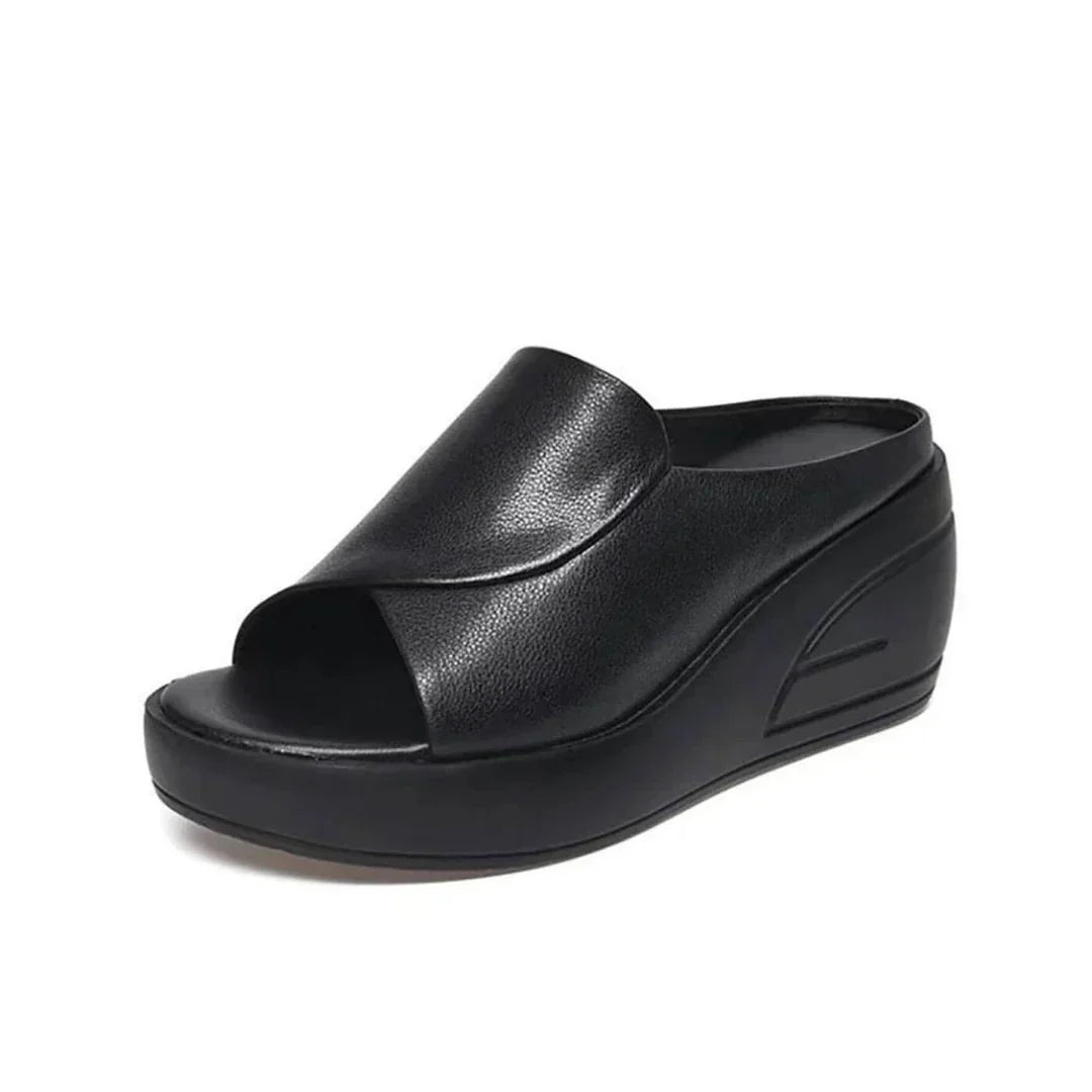Black orthopedic slip-on wedge sandal with a smooth curved strap, displayed in a studio setting.