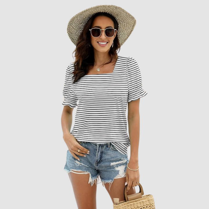 Woman in black-striped top, denim shorts, straw hat, carrying woven bag. Studio background enhances look.