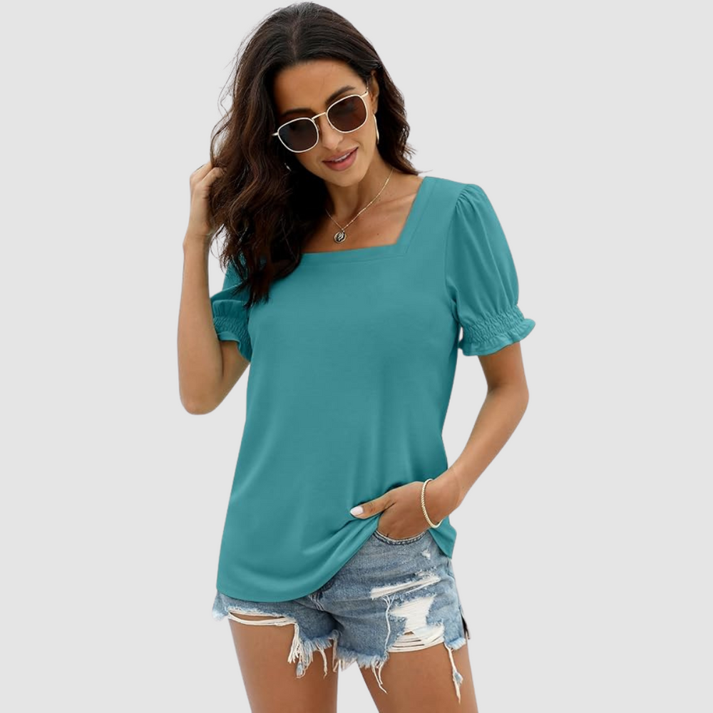 Woman in teal square neck top with gathered sleeves, denim shorts, sunglasses. Studio background provides clean visual.