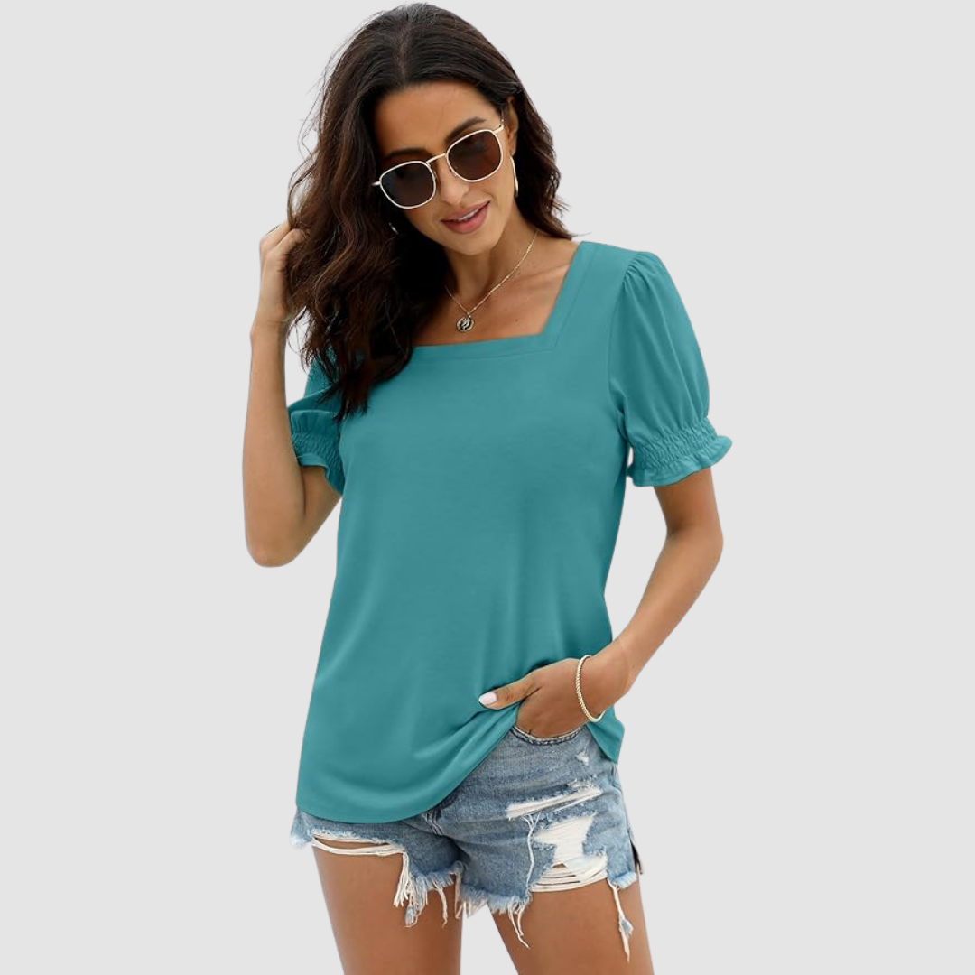 Woman in teal square neck top with gathered sleeves, denim shorts, sunglasses. Studio background provides clean visual.