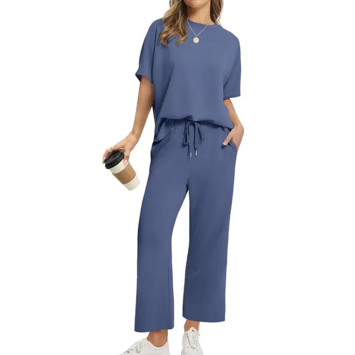 Woman styled in a sophisticated blue set with loose top and drawstring pants, holding a coffee, studio backdrop.