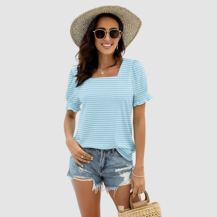 Woman in light blue striped top, denim shorts, straw accessories. Studio shot offers clear view of outfit.