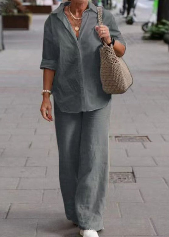 Woman in gray two-piece set with folded cuffs, walking while carrying a beige woven bag on a sidewalk.