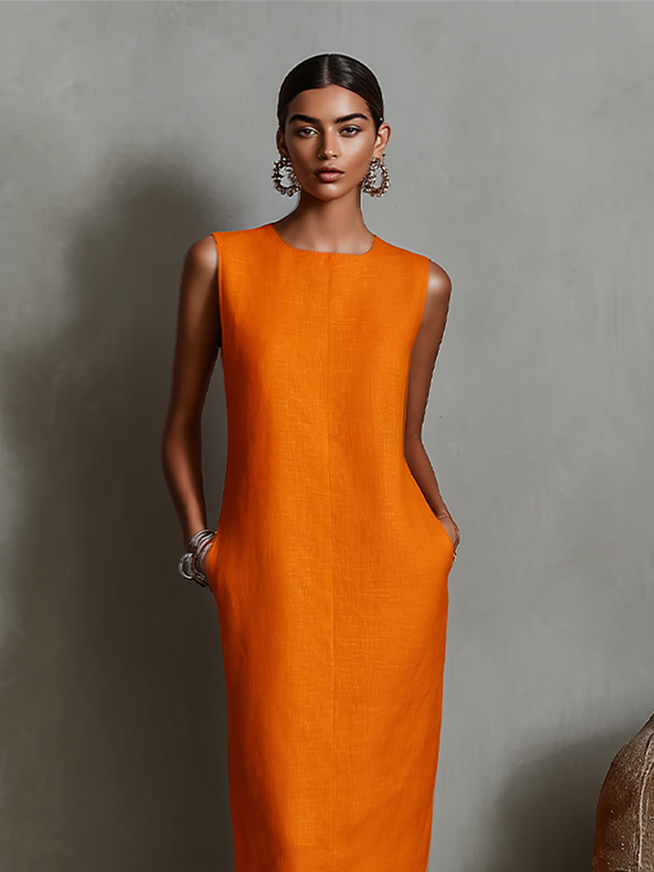 Close-up view of orange midi dress with pockets, sleeveless, modeled in studio with textured background.