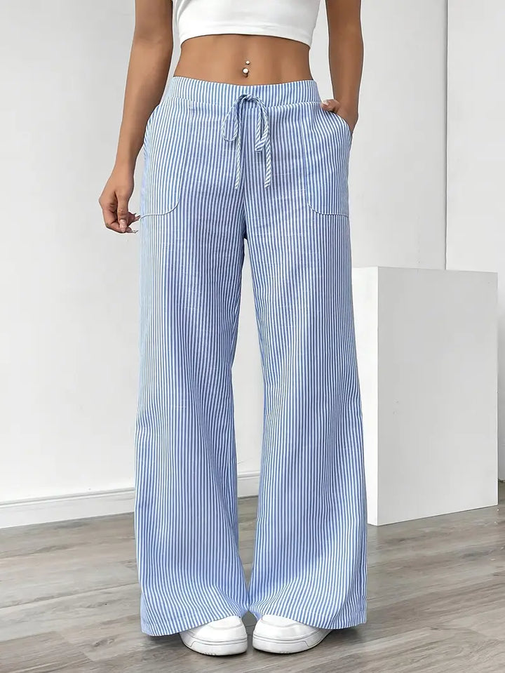 Blue and white striped relaxed pants with drawstring waist, displayed indoors, paired with white sneakers and crop top.