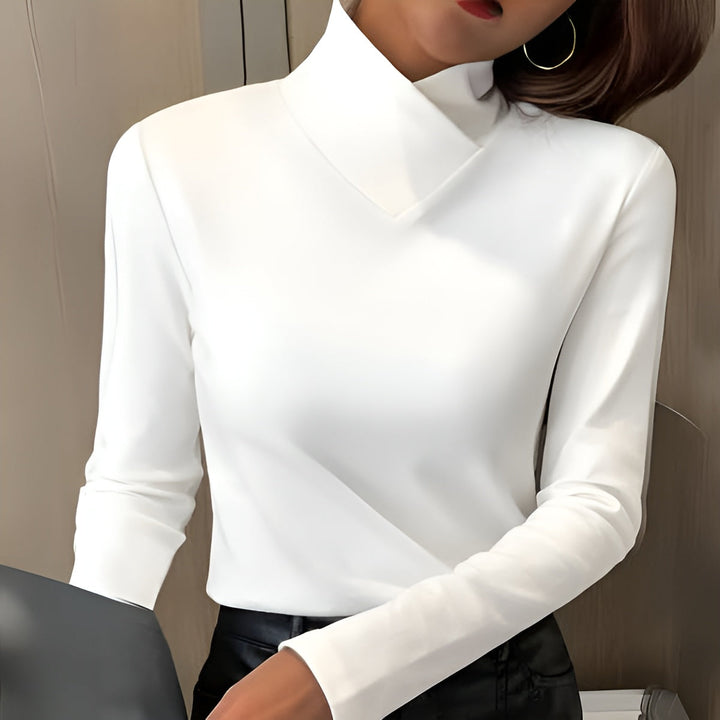 White high-neck sweater with long sleeves, worn indoors. Neutral-toned background with subtle lighting.