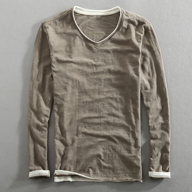 Beige long sleeve shirt with white trim, laying flat on a gray surface.