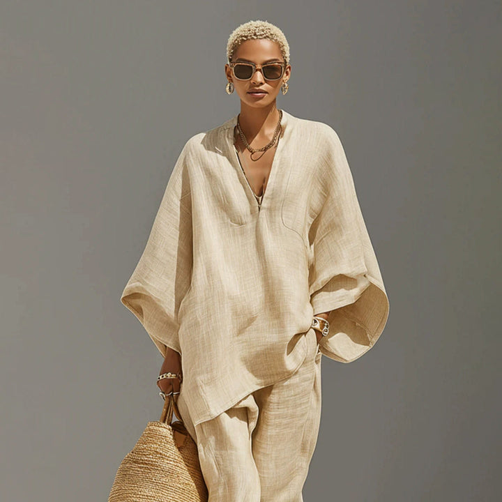 Model in beige batwing sleeve V-neck lounge set carrying woven bag, studio background.