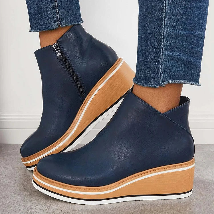 Navy blue luxe boots with wedge sole and zipper, paired with frayed jeans, on a gray floor and white wall.