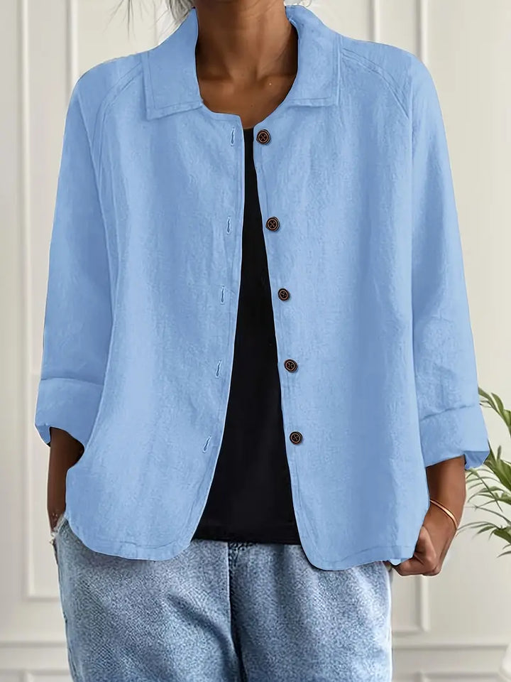 Light blue button-up top with rolled sleeves, worn over black shirt in an indoor setting.