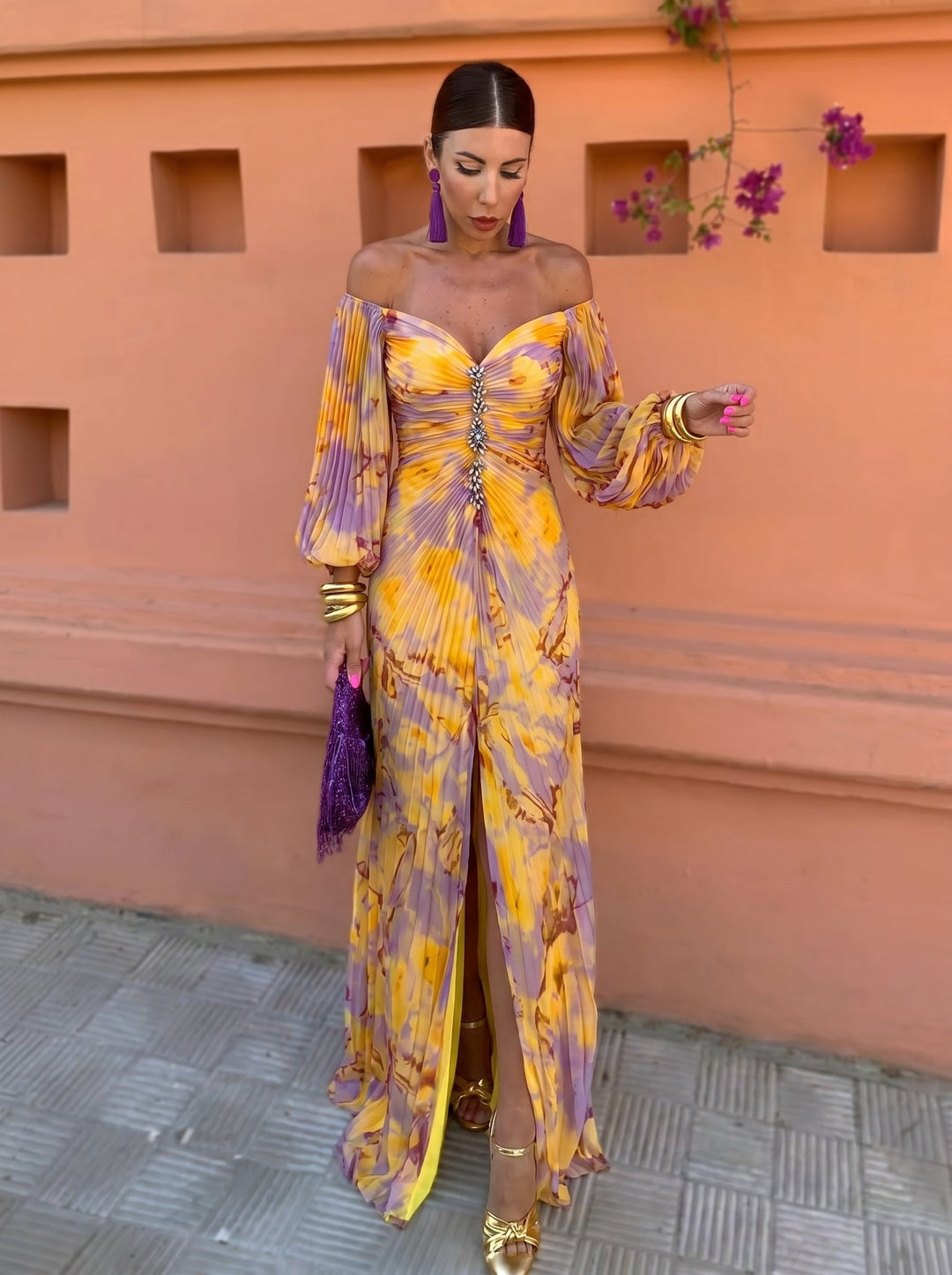 Woman in a long floral dress with a deep neckline and off-shoulder sleeves, against an orange backdrop with flowers.