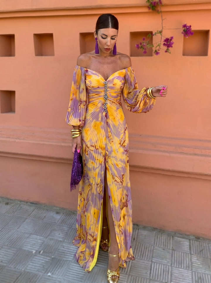 Woman in a long floral dress with a deep neckline and off-shoulder sleeves, against an orange backdrop with flowers.