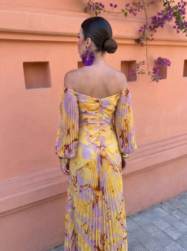Back view of a floral dress with ruched detail, against an orange wall with hanging purple flowers.