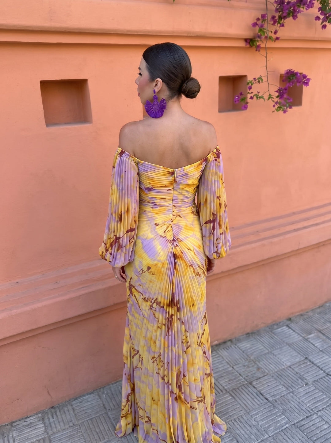 Rear view of a colorful floral dress with a ruched back, placed against a floral-accented orange wall.