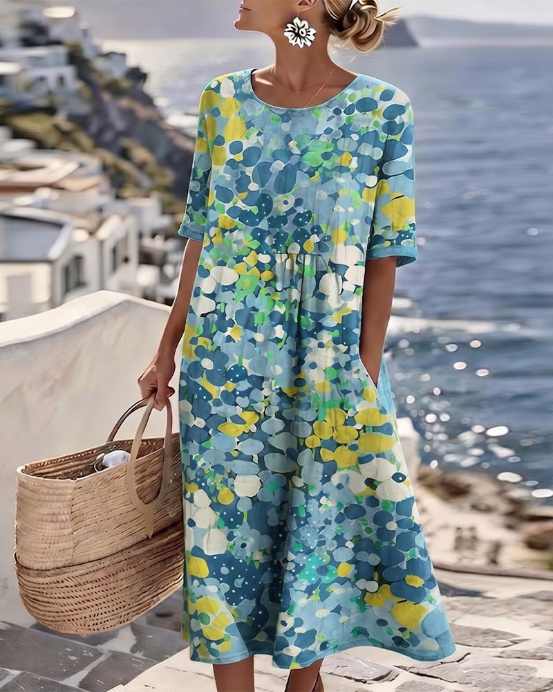 Woman in blue floral midi dress, holding wicker bag on sunny coastal terrace with ocean view.