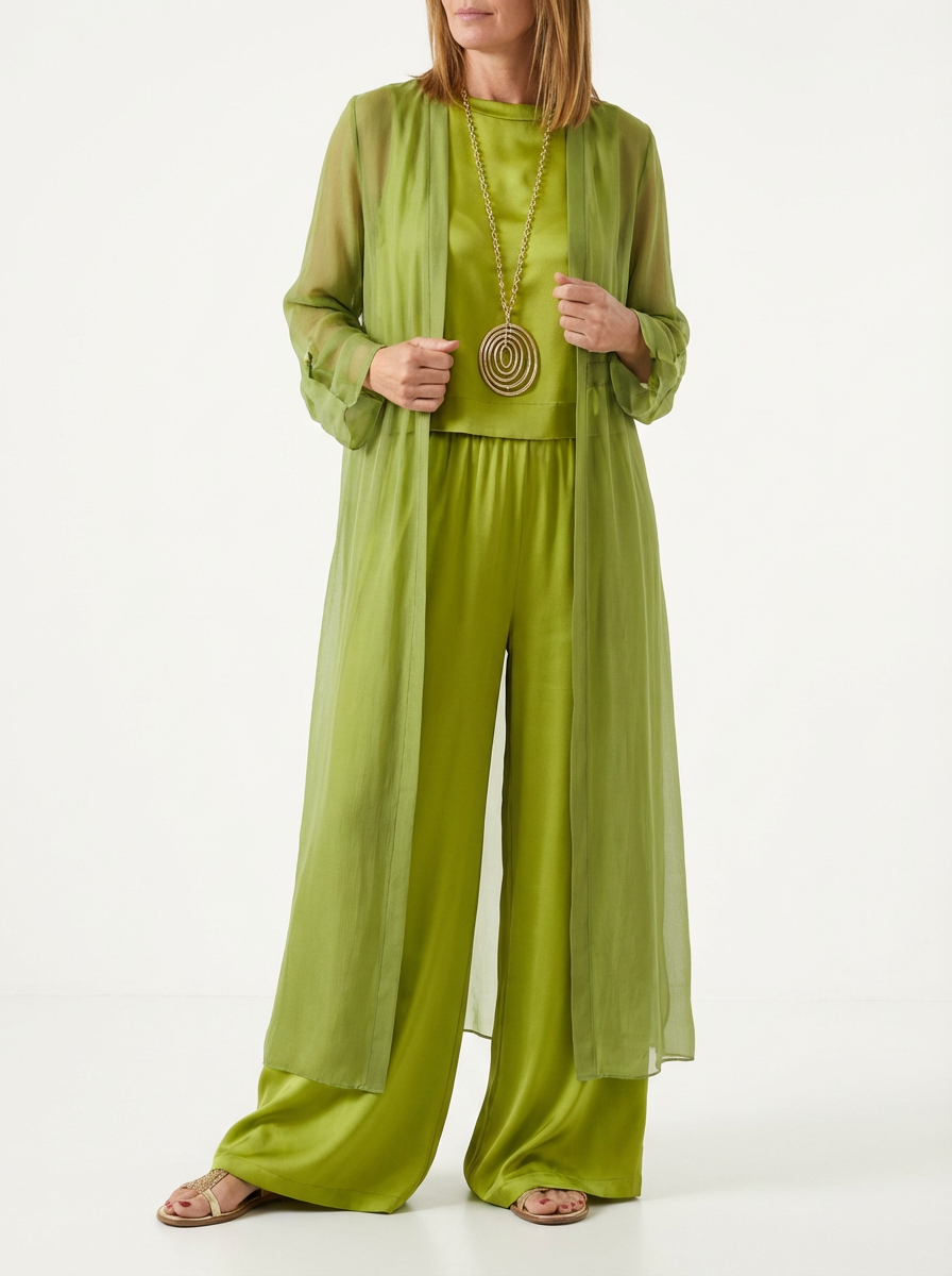 Model wearing olive green three-piece set featuring a sheer long duster, sleeveless top, wide-leg pants, gold necklace, and sandals in minimal studio background.